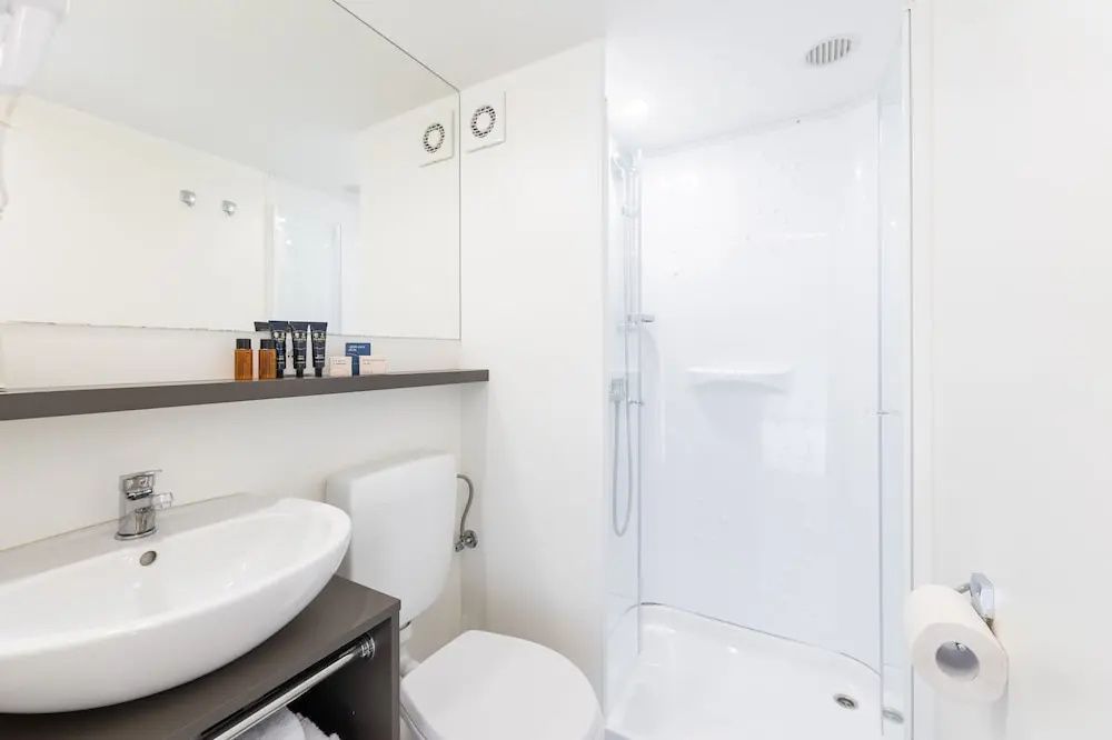 Helles modernes Badezimmer mit weißem Waschbecken, Toilette und einer geräumigen Dusche.