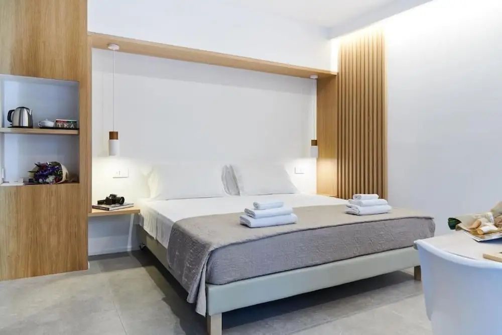 Modernes Doppelbett mit weißer Bettwäsche, Holzdekor an der Wand und hängenden Lampen.
