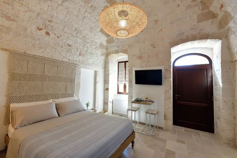 Gewölbe-Schlafzimmer mit Doppelbett, Wand-TV, kleinem Bistrotisch und Holzeingangstür.