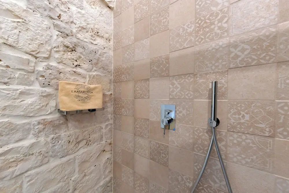 Duschbereich mit beige gemusterten Fliesen, Handbrause und Natursteinmauerwerk.