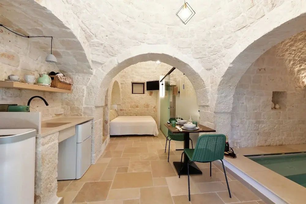Blick in die Suite mit Steinbögen, Küchenzeile, Esstisch und Bett im Hintergrund.