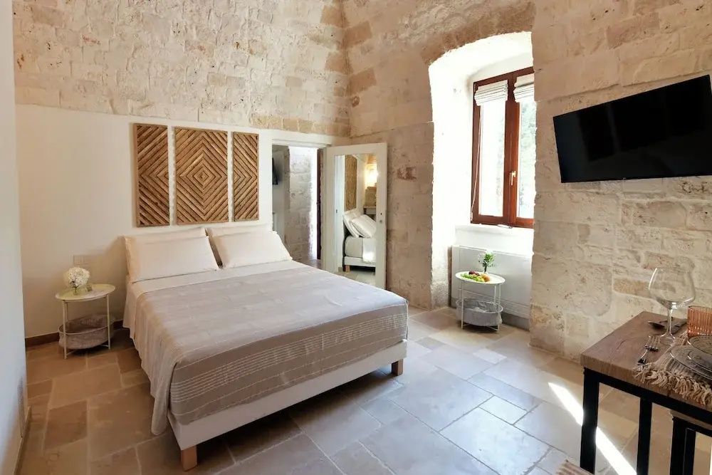 Hell eingerichtetes Schlafzimmer mit Doppelbett, Steingewölbewänden und Wanddekoration.