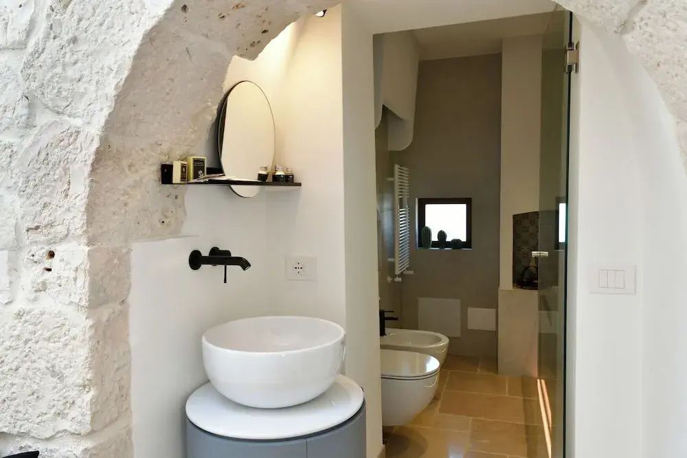 Modernes Badezimmer mit rundem Aufsatzwaschbecken und Spiegel unter einem Steinbogen.