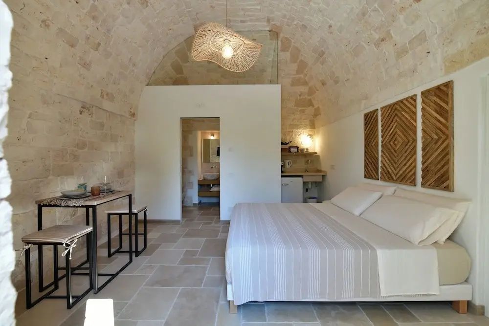 Schlafzimmer mit einem Gewölbe aus Naturstein, hellem Fliesenboden und einem Doppelbett.