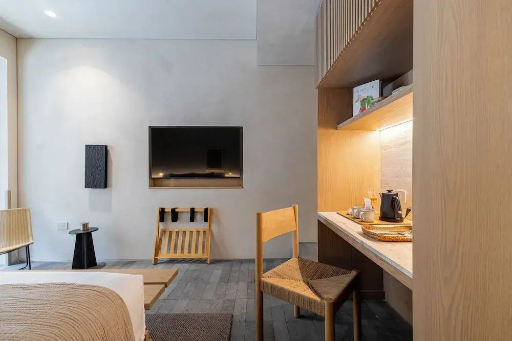 Schreibtisch aus Holz mit Stuhl und Kaffeestation sowie Fernseher an der hellen Wand im Hotelzimmer.