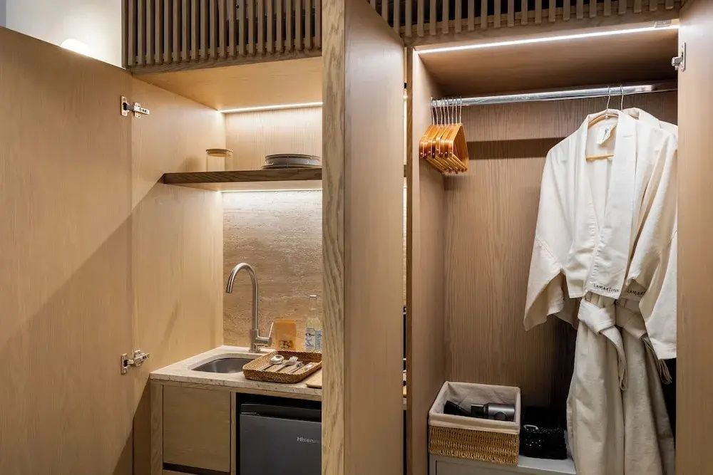 Offener Holzschrank mit integrierter Küchenzeile, Spülbecken, Minibar und Kleiderstange mit Bademantel.