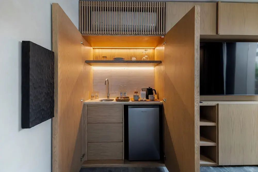 In einem Holzschrank integrierte Kitchenette mit kleinem Kühlschrank, Waschbecken und Wasserkocher.