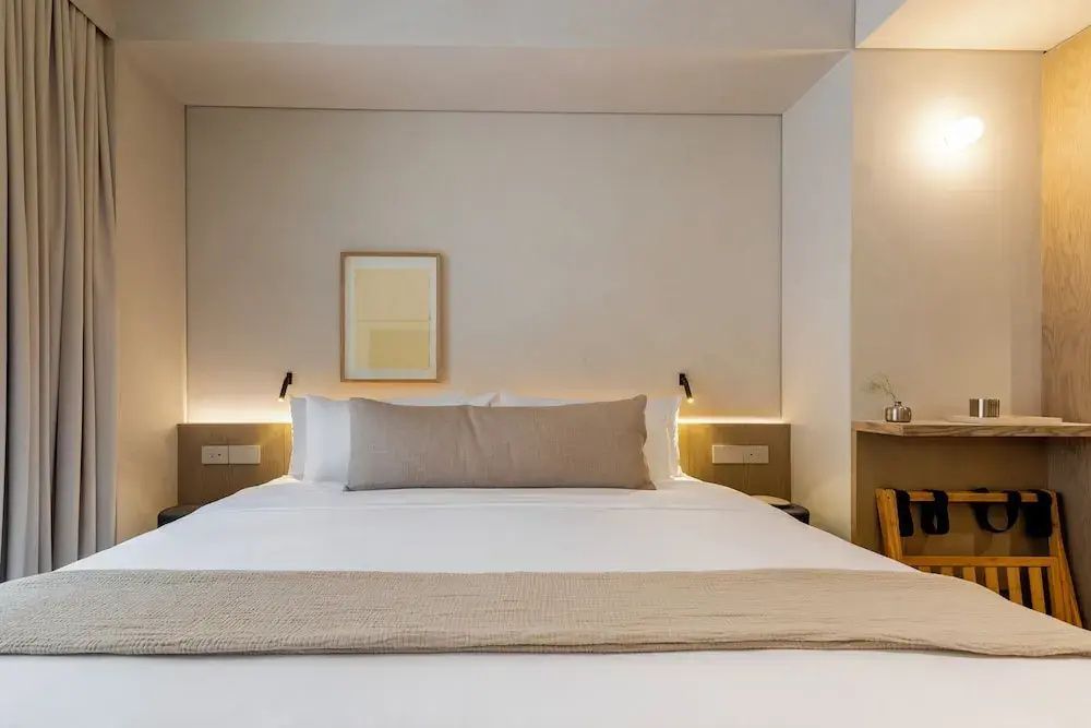 Großes Doppelbett mit beigem Kissen und indirekter Wandbeleuchtung.