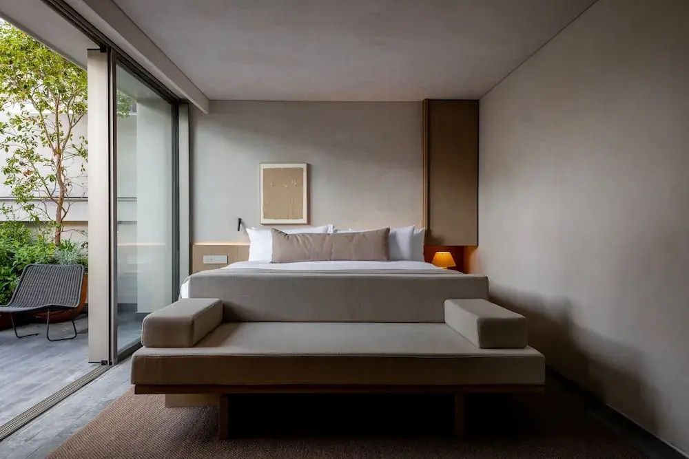 Hell eingerichtetes Schlafzimmer mit Doppelbett, gepolsterter Bank und Zugang zur Terrasse.