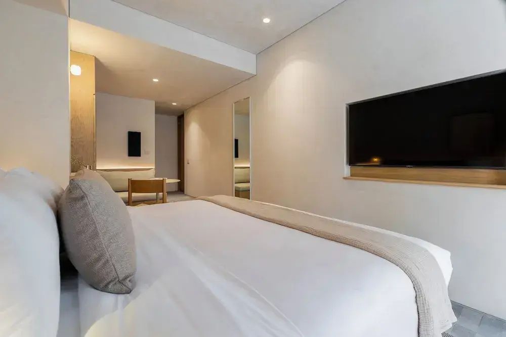 Blick vom Bett auf einen Flachbildfernseher an der weißen Zimmerwand.