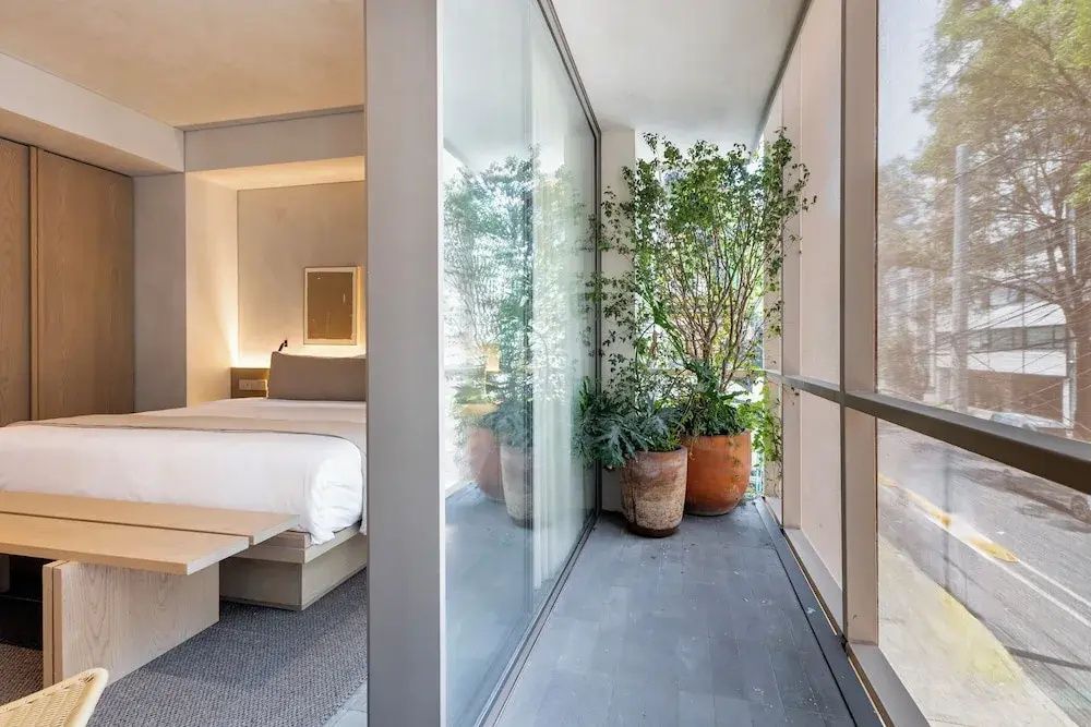 Modernes Hotelzimmer mit hellen Tönen und angrenzendem verglastem Balkon mit Pflanzen.