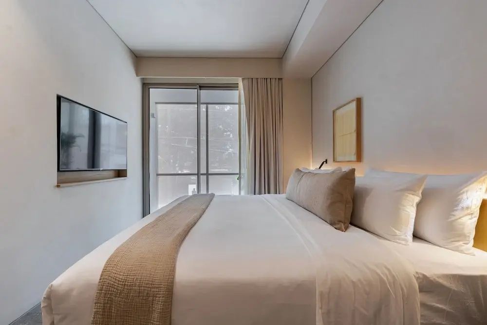 Helles Hotelzimmer mit großem Doppelbett, Flachbildfernseher an der Wand und Zugang zum Balkon.