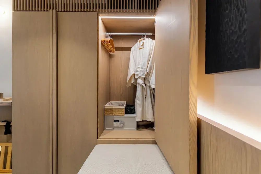 Offener Holzkleiderschrank mit einem weißen Bademantel, Hängern und einem kleinen Safe.
