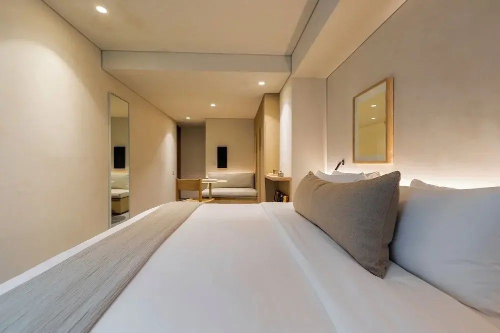 Modernes Hotelzimmer mit großem Doppelbett, neutralen Tönen und einem Sitzbereich im Hintergrund.