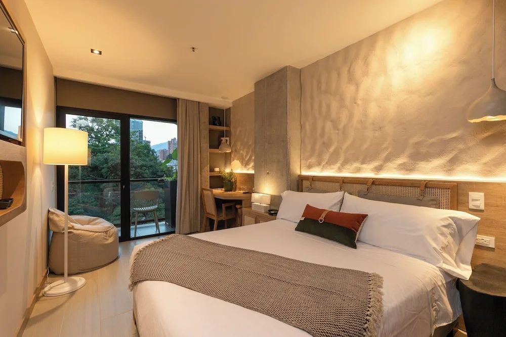Doppelbett im Hotelzimmer mit Holztisch und Blick auf den Balkon.