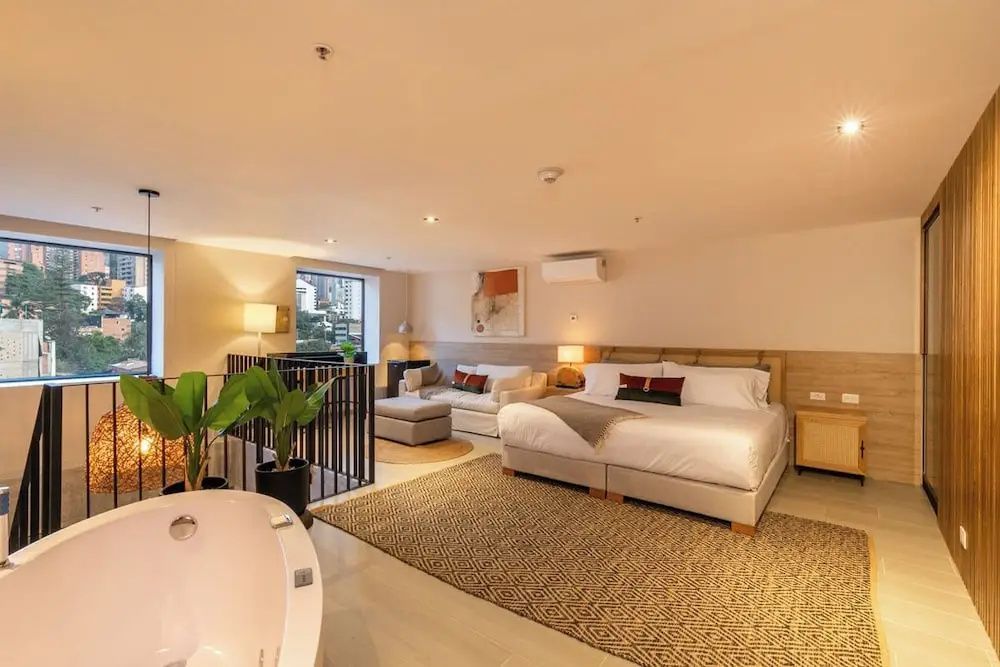 Geräumiges Hotelzimmer mit Doppelbett, hellem Sofa, Teppich und frei stehender Badewanne.