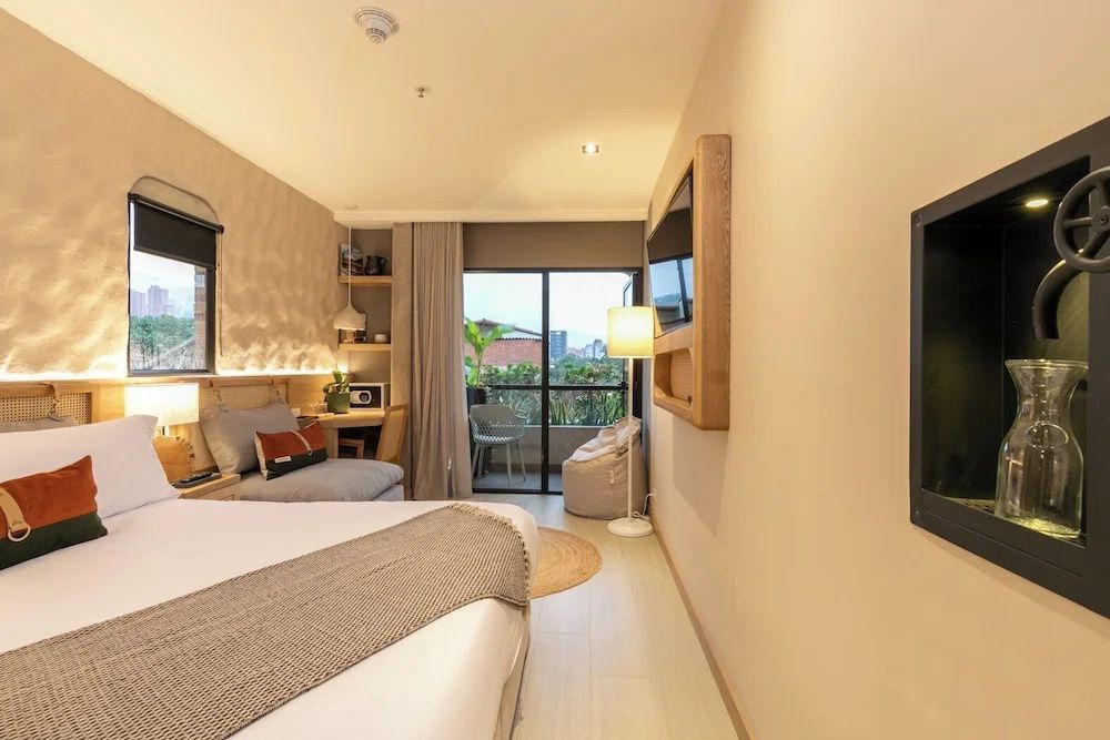 Hell eingerichtetes Hotelzimmer mit Doppelbett, Fernseher und Balkonzugang.
