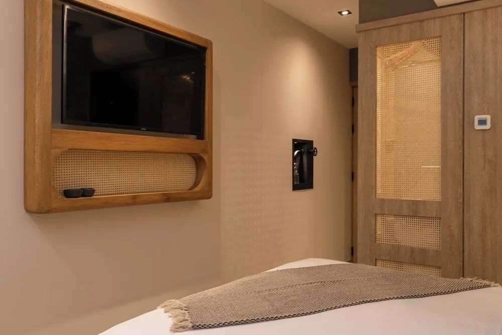 Wandbereich im Hotelzimmer mit Fernseher, Schrank aus Rattan und Bett.