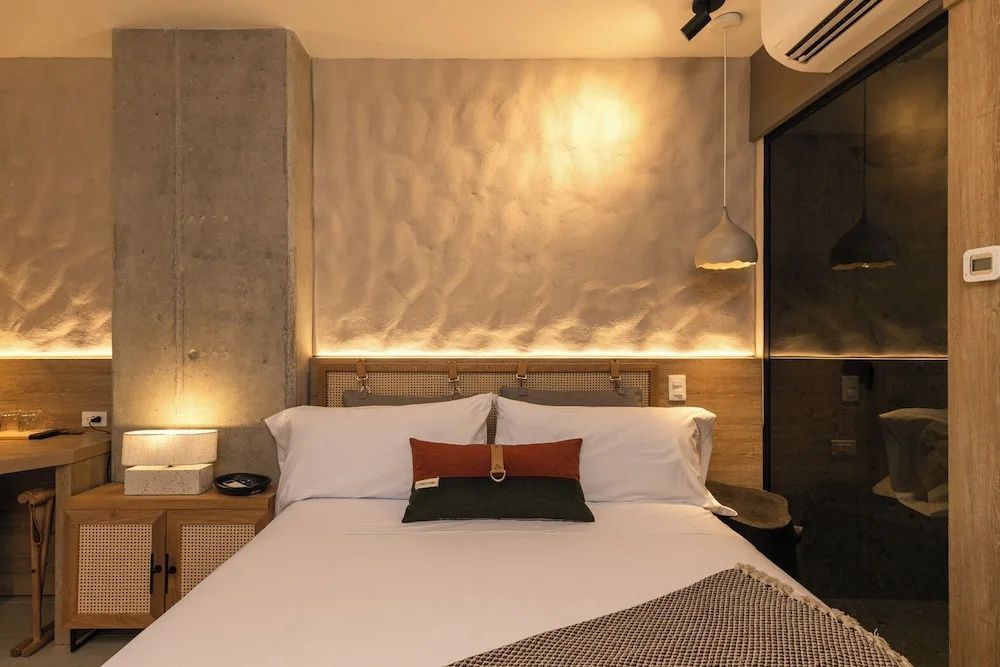 Doppelbett mit weißer Bettwäsche, bunten Kissen und indirekter Beleuchtung an der Rückwand.
