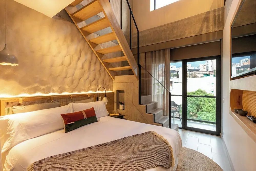 Zimmer über zwei Etagen mit Holztreppe, Doppelbett und großem Fenster zum Balkon.