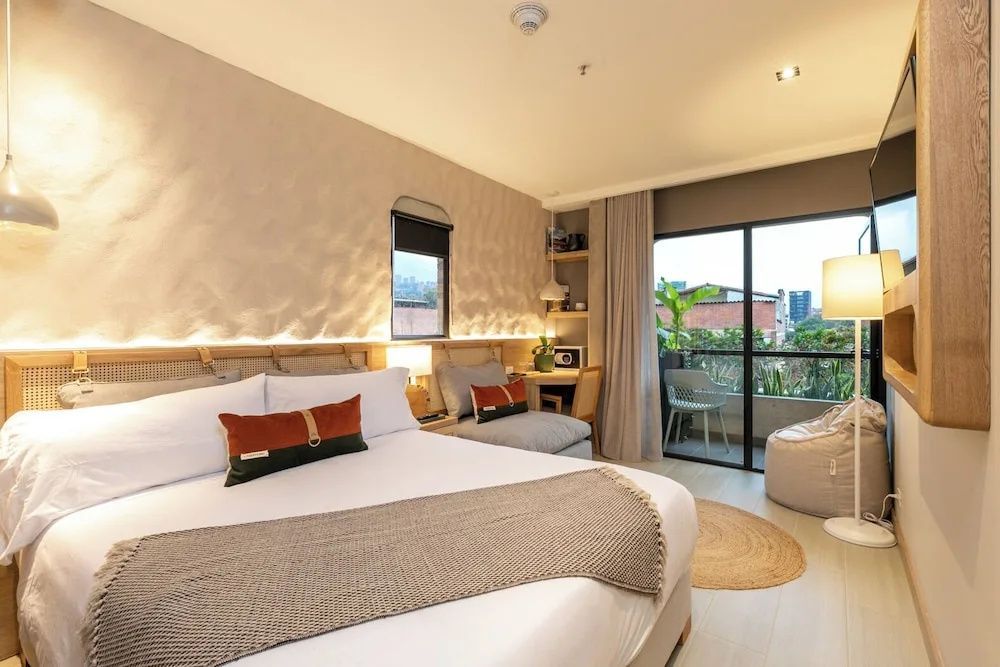 Großes Doppelbett mit braunen Kissen und Blick auf Balkon und Schreibtisch.
