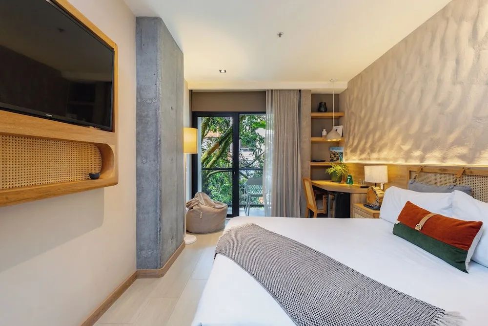 Hotelzimmer mit weißem Doppelbett, Fernseher an der Wand und Balkonzugang ins Grüne.