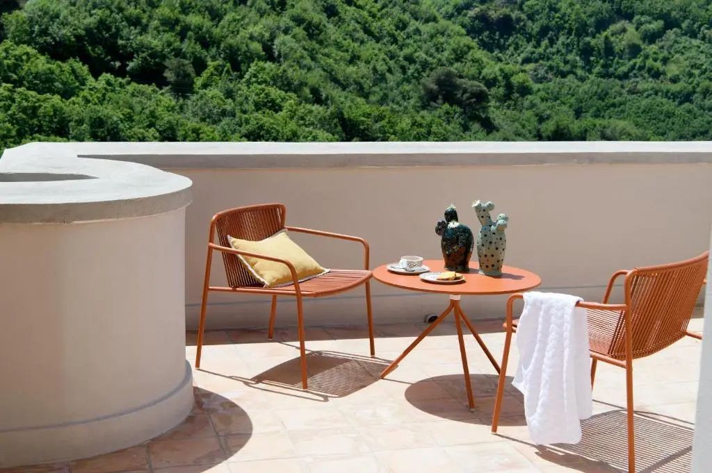 Sonnige Terrasse mit orangefarbenen Balkonmöbeln und Blick auf bewaldete Hügel in der Umgebung.