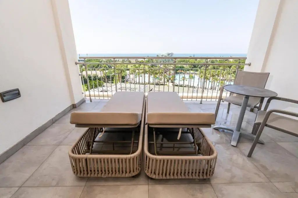 Zwei Sonnenliegen auf einem Hotelbalkon mit Blick auf die Gartenanlage und das Meer.
