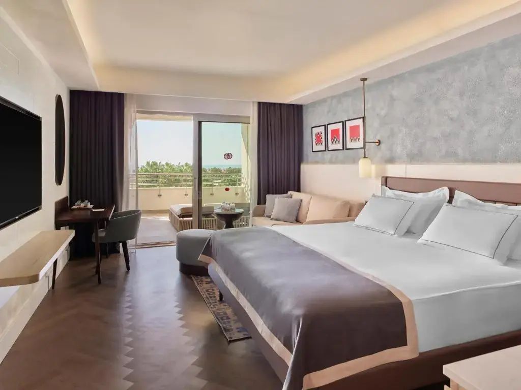 Geräumiges Hotelzimmer mit großem Doppelbett, Sofa und Balkon mit Aussicht.