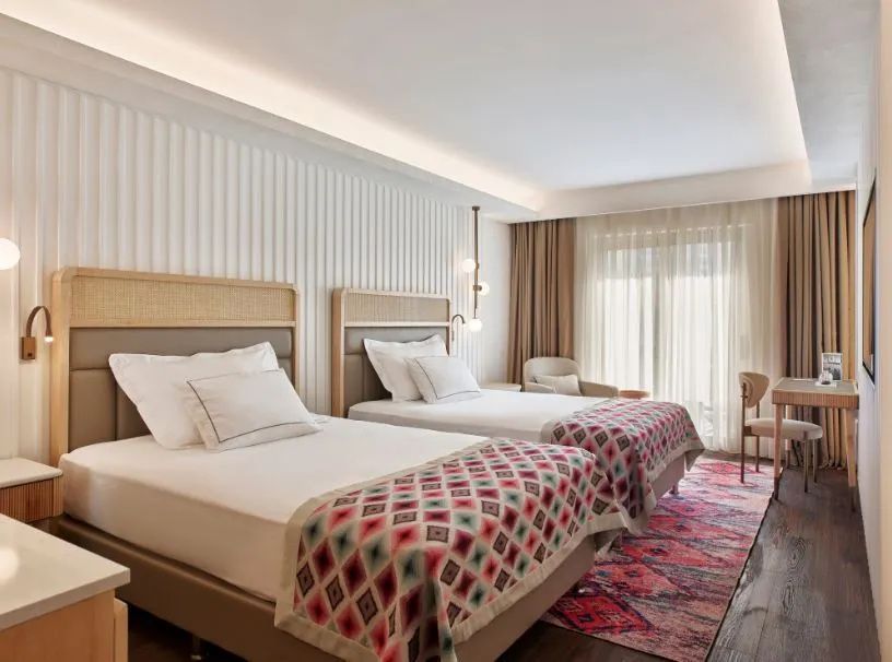 Zwei Einzelbetten mit gemusterten Decken in einem hell eingerichteten Hotelzimmer.
