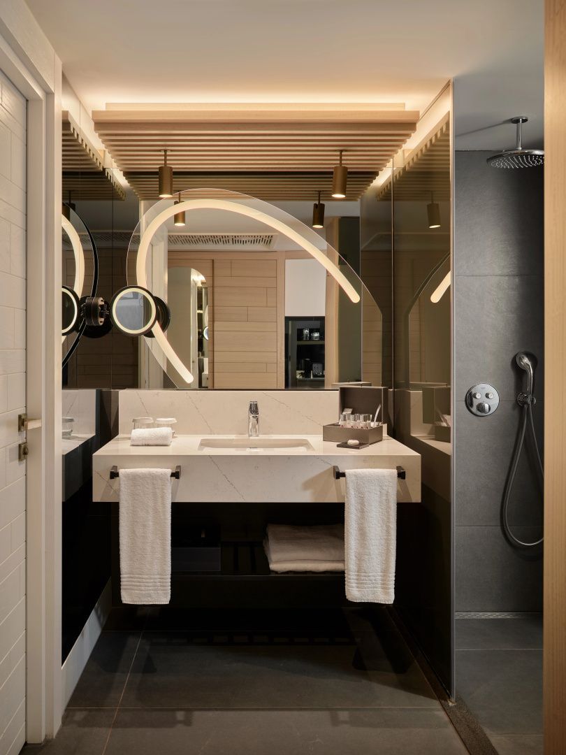 Modernes Badezimmer mit beleuchtetem Spiegel, Waschbecken und angrenzender Dusche.