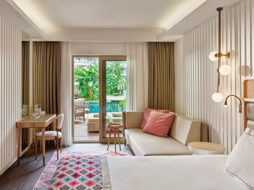 Modernes Hotelzimmer mit hellen Wänden, Sofa, Schreibtisch und Terrassentür.