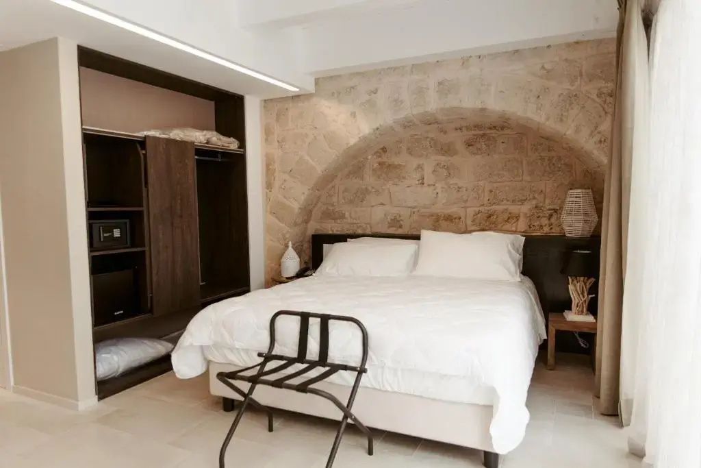 Hotelzimmer mit Doppelbett unter einem Natursteinbogen und dunklem Kleiderschrank.