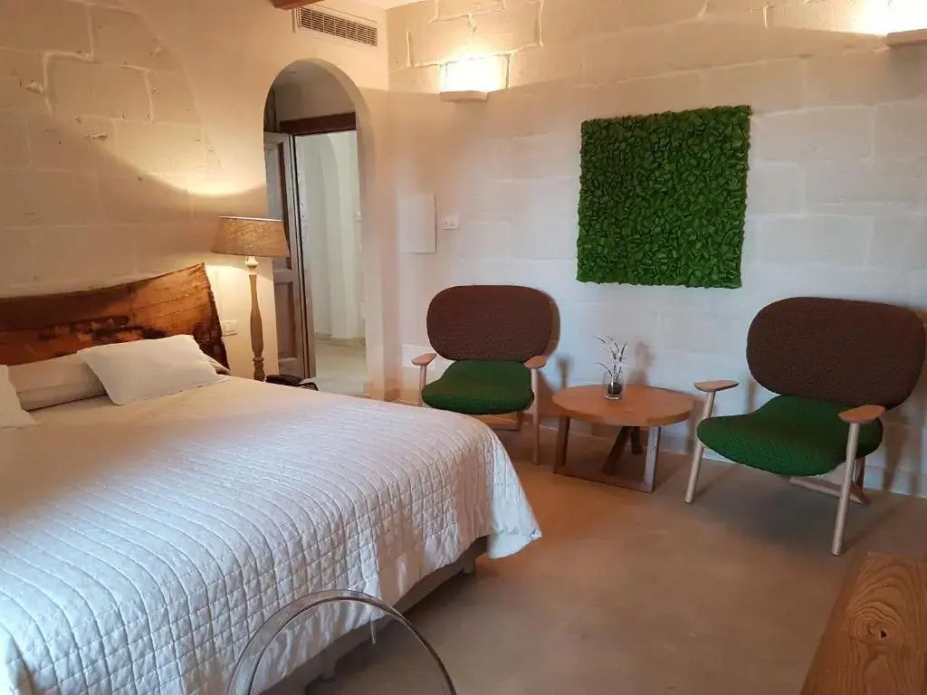 Helles Schlafzimmer mit Doppelbett, Holzdekoration, zwei Sesseln und Pflanzenbild an der Wand.