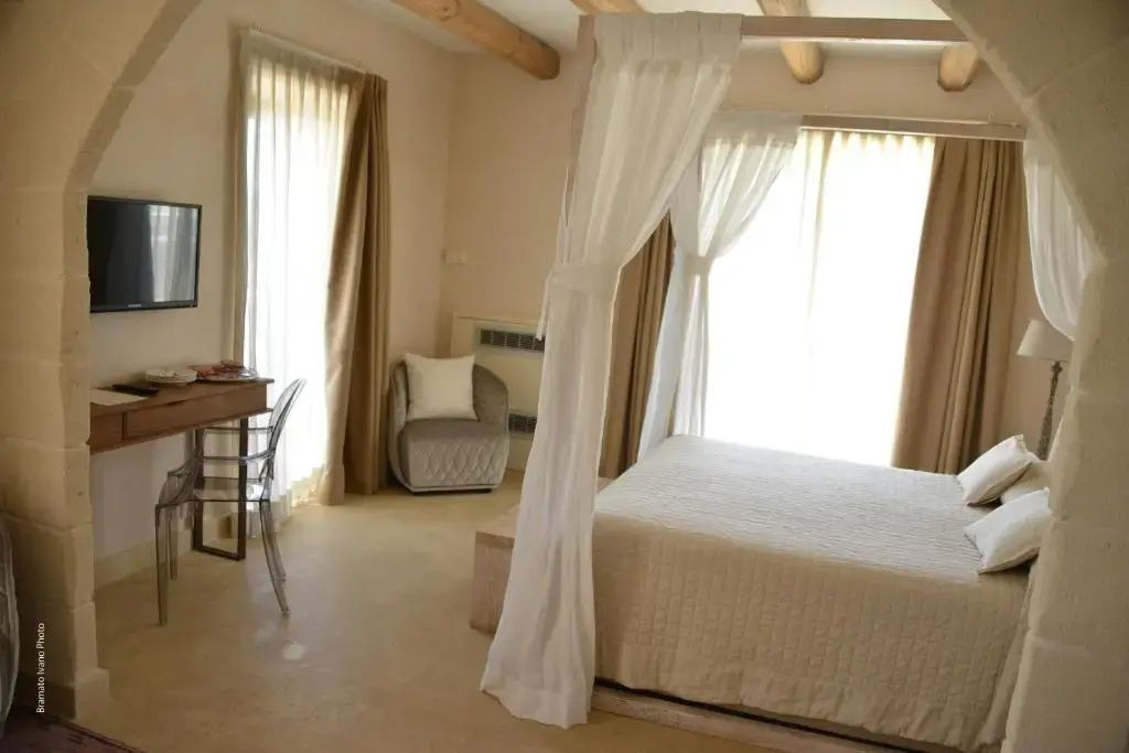 Helles Hotelzimmer mit einem Himmelbett, Holzbalken an der Decke und einem Sessel.