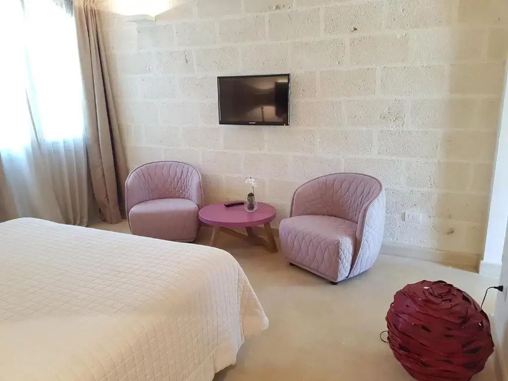 Sitzbereich im Hotelzimmer mit zwei rosa Sesseln, lila Beistelltisch und Fernseher an der Wand.