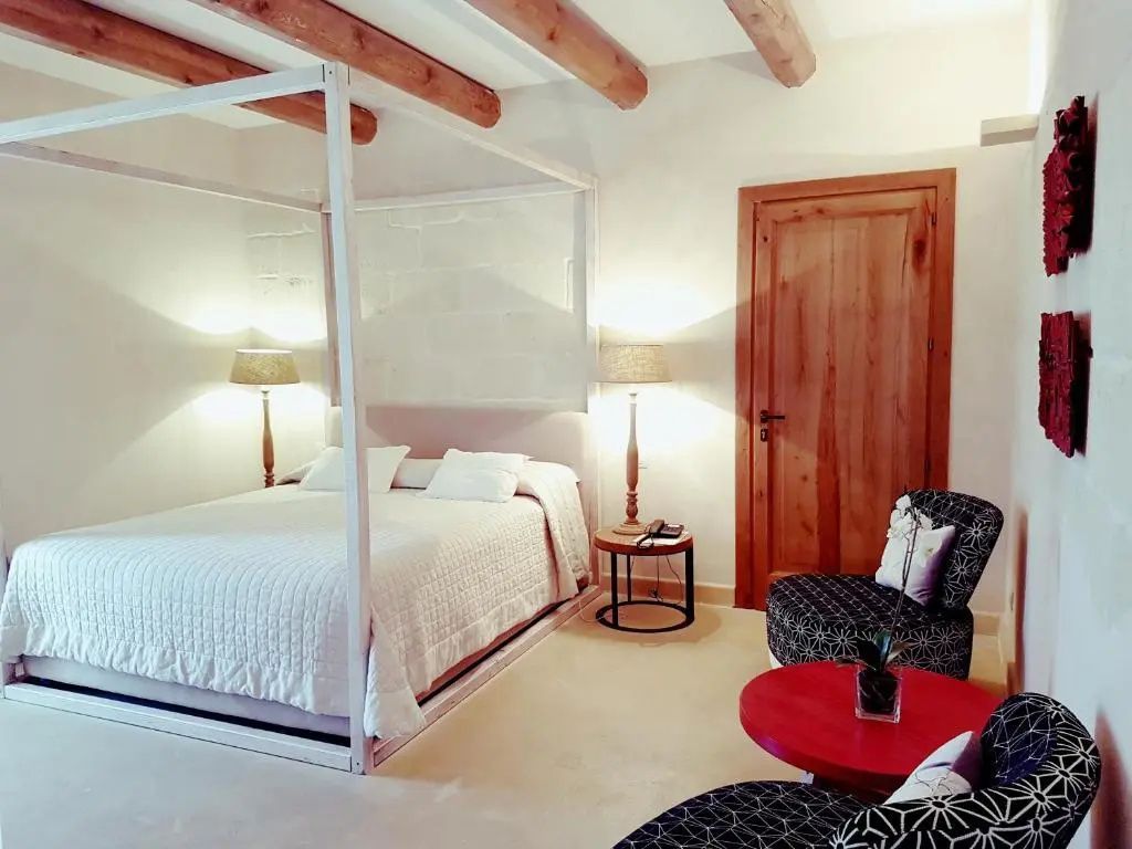 Schlafzimmer mit weißem Himmelbett, zwei Stehlampen, Sessel und rotem Beistelltisch.