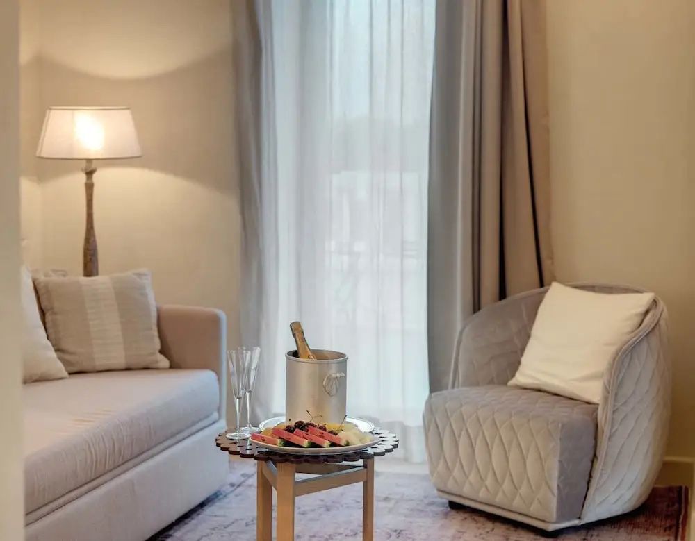 Sitzecke in neutralen Farben mit grauem Sessel, beigem Sofa und Beistelltisch vor hellen Vorhängen.