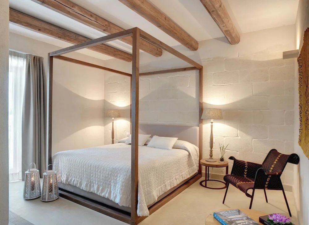 Himmelbett aus dunklem Holz in einem Zimmer mit hellen Steinwänden und Tischlampen.