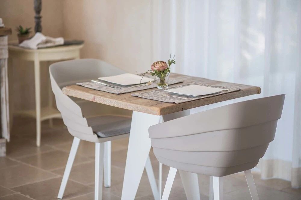 Gedeckter Holztisch für zwei Personen mit grauen Stühlen und kleiner Blumendekoration.