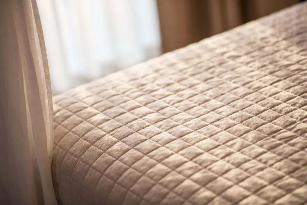 Nahaufnahme einer gesteppten beigefarbenen Tagesdecke auf einem Bett.