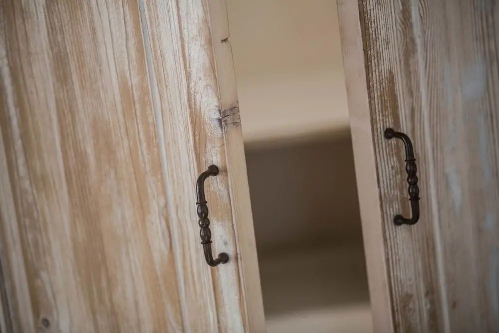 Nahaufnahme von zwei leicht geöffneten Schranktüren aus hellem Holz mit Metallgriffen.