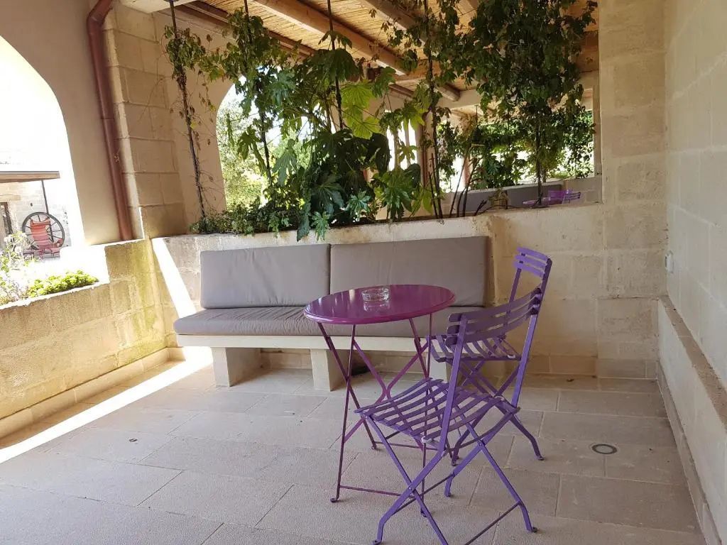 Überdachte Terrasse mit lila Klapptisch, Stühlen und einer Steinbank vor einer Pflanzwand.