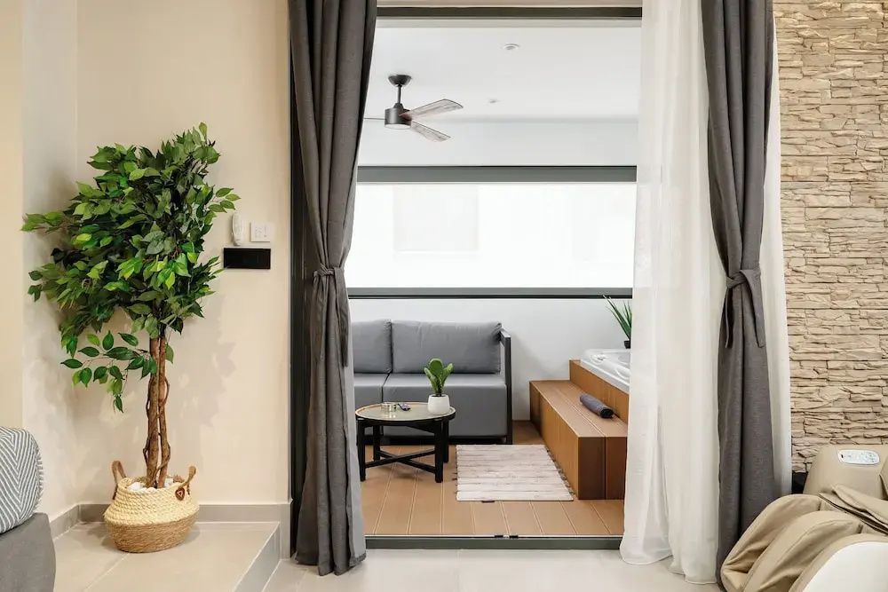 Wohnbereich mit grauem Sofa, kleinem Tisch und Podest mit Whirlpool hinter Vorhängen.