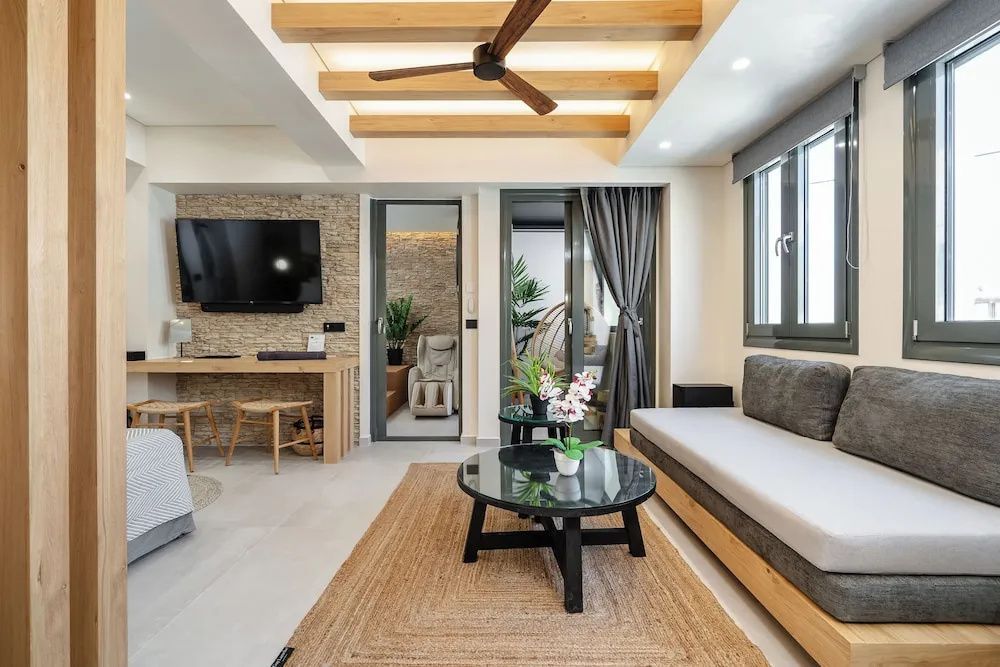 Modernes Wohnzimmer mit hellem Sofa, braunem Couchtisch und Fernseher an einer Natursteinwand.