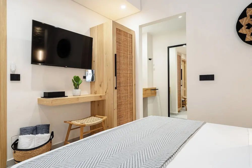 Modern eingerichtetes Hotelzimmer mit Holzschrank, Fernseher und kleinem Hocker.