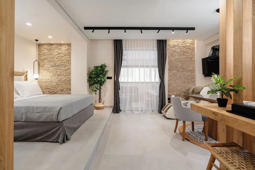Offenes Hotelzimmer mit Doppelbett, Natursteinwand, Schreibtisch und Sitzgelegenheiten.