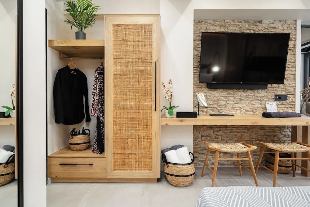 Offener Kleiderschrank aus Holz mit Geflecht und Schreibtisch mit Wandfernseher.