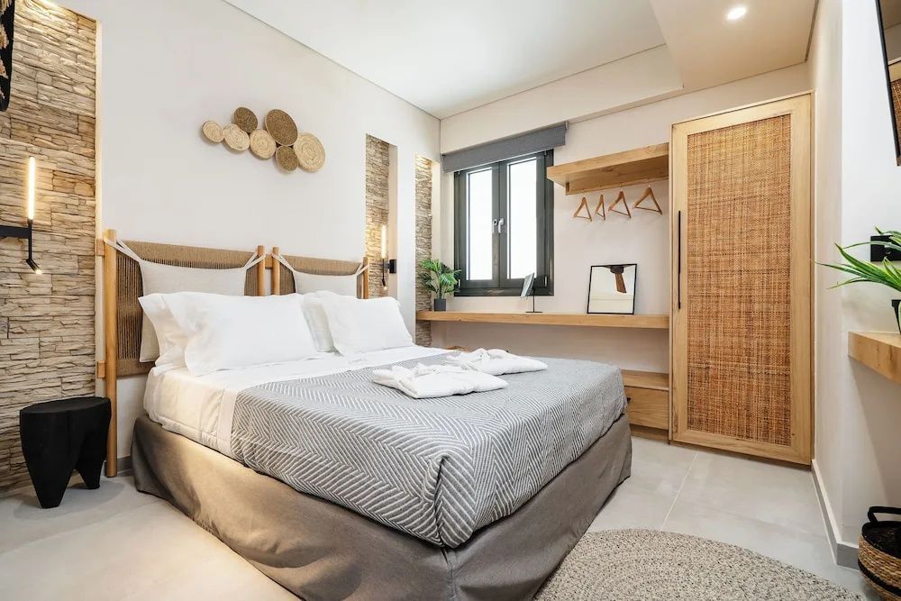 Doppelbett mit grauer Tagesdecke und weißer Bettwäsche neben Holzschrank und Fenster.