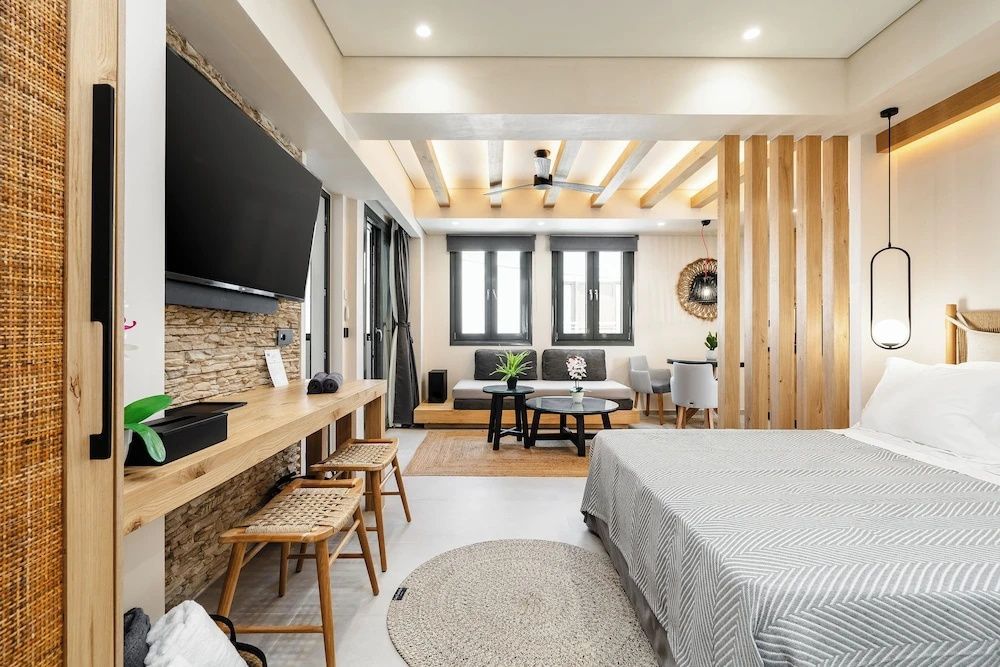 Offener Wohn- und Schlafbereich mit Bett, Fernseher an Natursteinwand und Holzdeckenbalken.